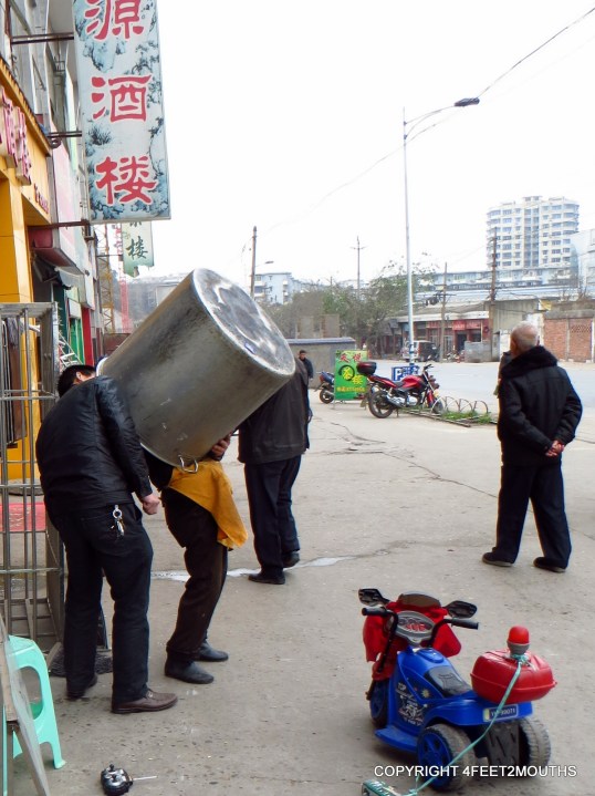 Two men clean a big pot on the street